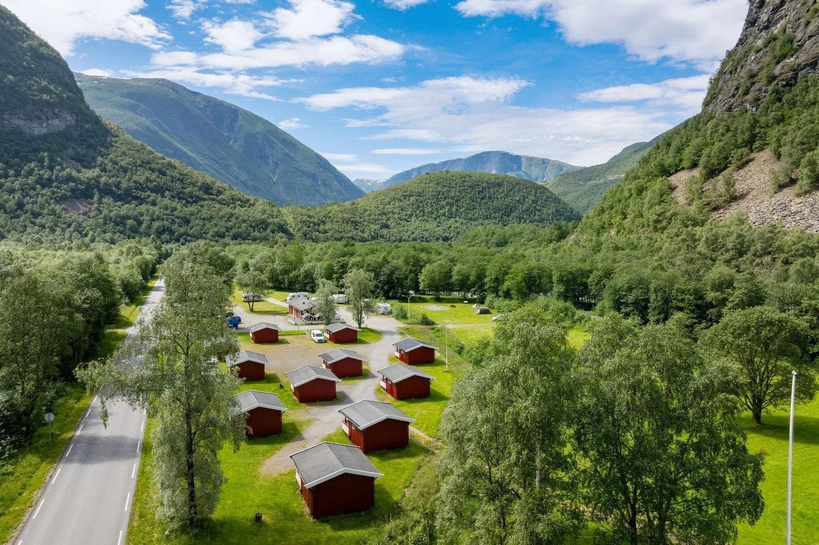 Red wooden cabins at Utladalen Camping surrounded by green trees and mountain walls